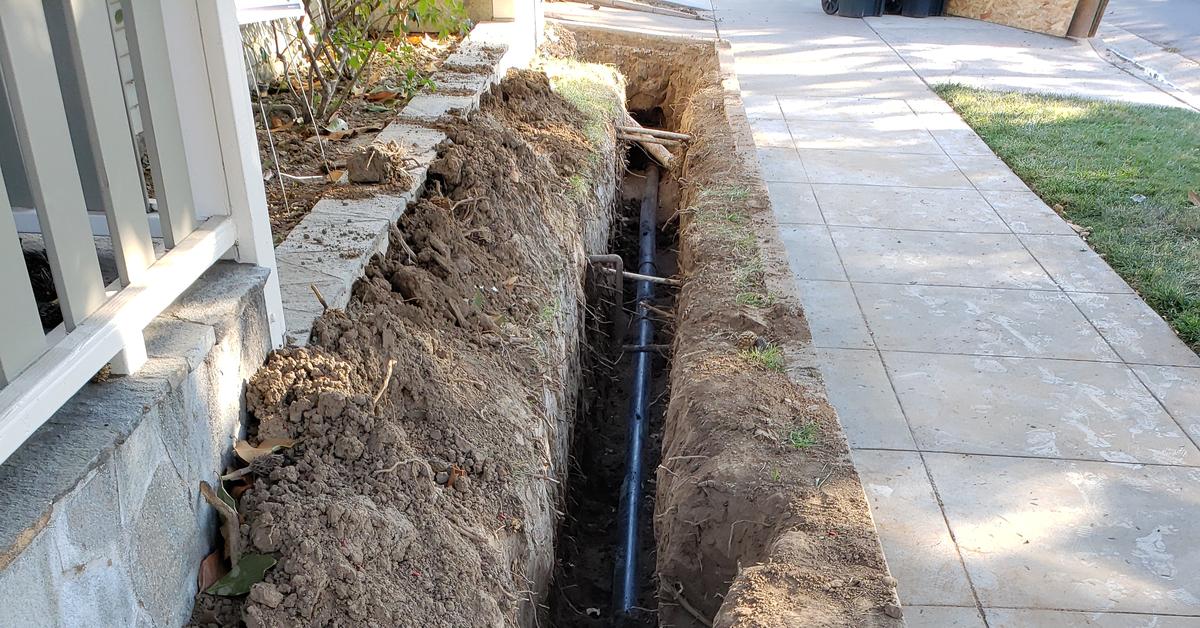 New sewer line installed in a side-yard trench between an Orange County home and the sidewalk, with a cleanout fitting in place