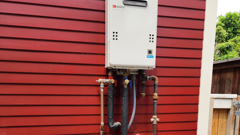 Exterior tankless water heater with copper gas and water manifold, installed in Orange County