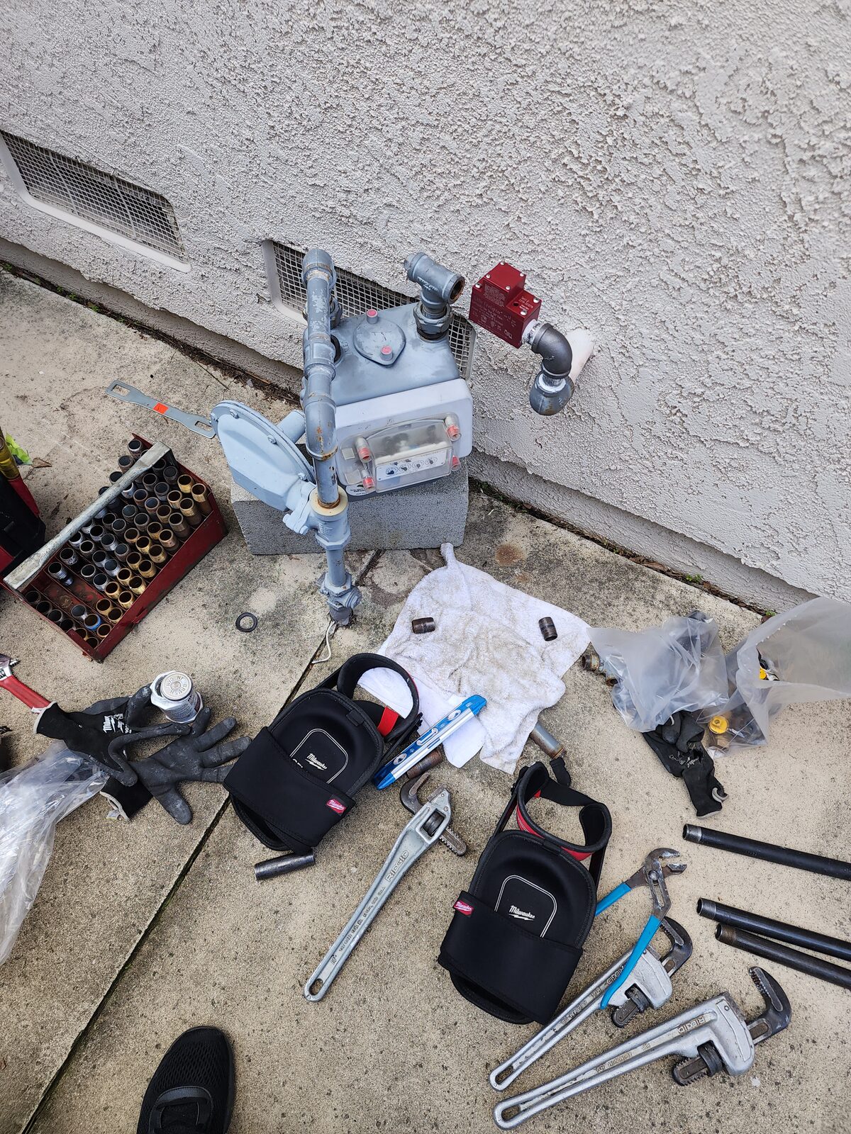 Professional Plumbing technician mid-install of an earthquake gas shutoff valve on an Orange County gas meter with pipe wrenches and tools staged on the ground