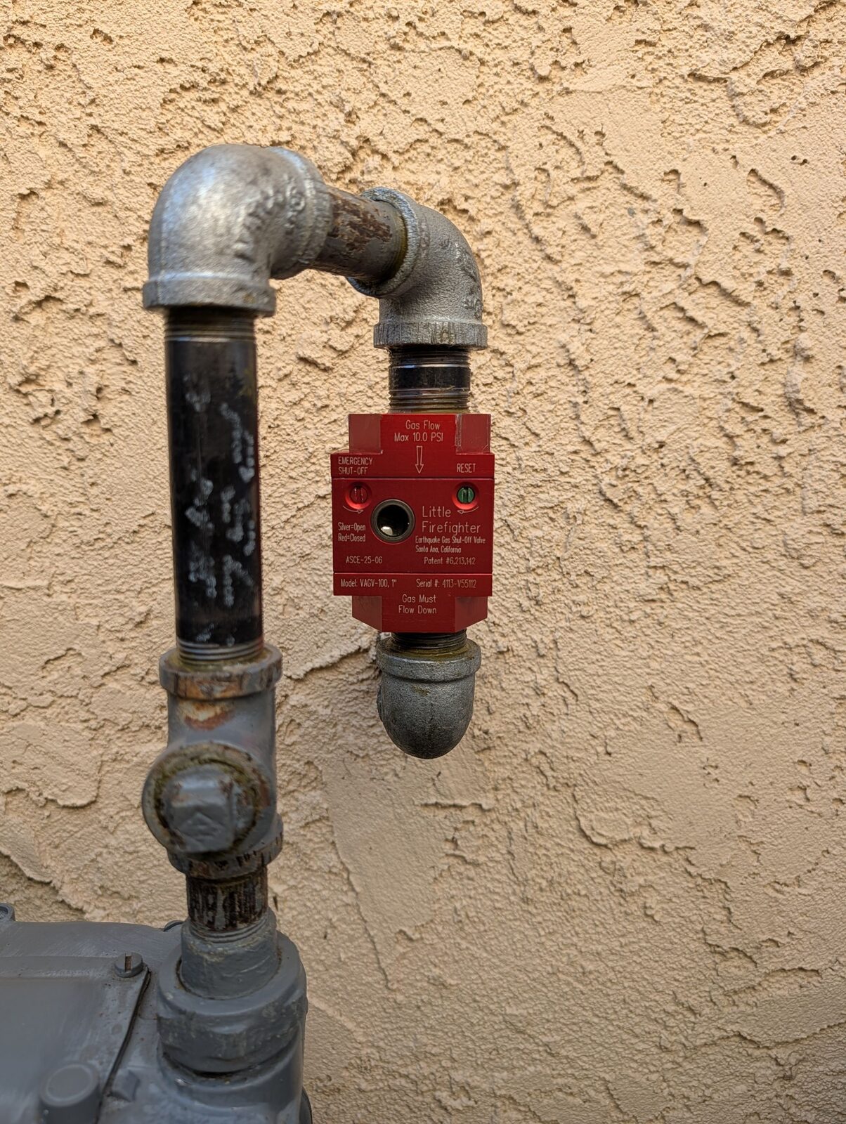 Close-up of a Little Firefighter earthquake gas shutoff valve on a Fountain Valley home showing the STOP and RESET screwdriver-slot markings on the valve housing