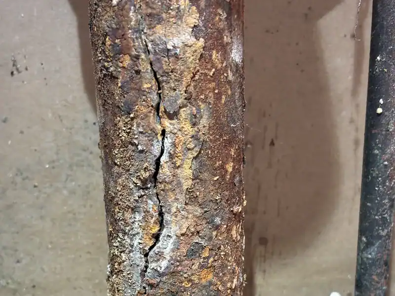 Close-up of a long crack running down a corroded cast iron drain pipe