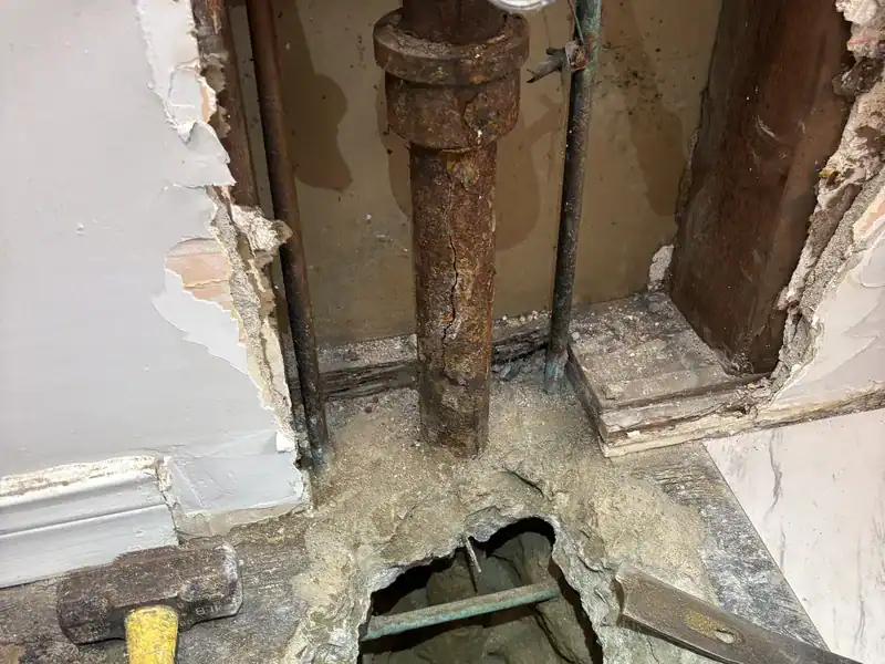 Floor opened around a cracked cast iron drain riser to reach the pipe for cast iron pipe replacement