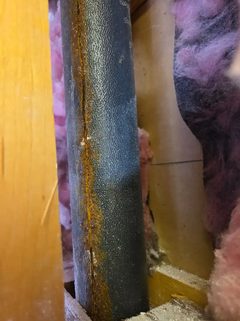 Corroded cast iron drain pipe with a rust seam, opened up inside the wall of a Newport Beach home